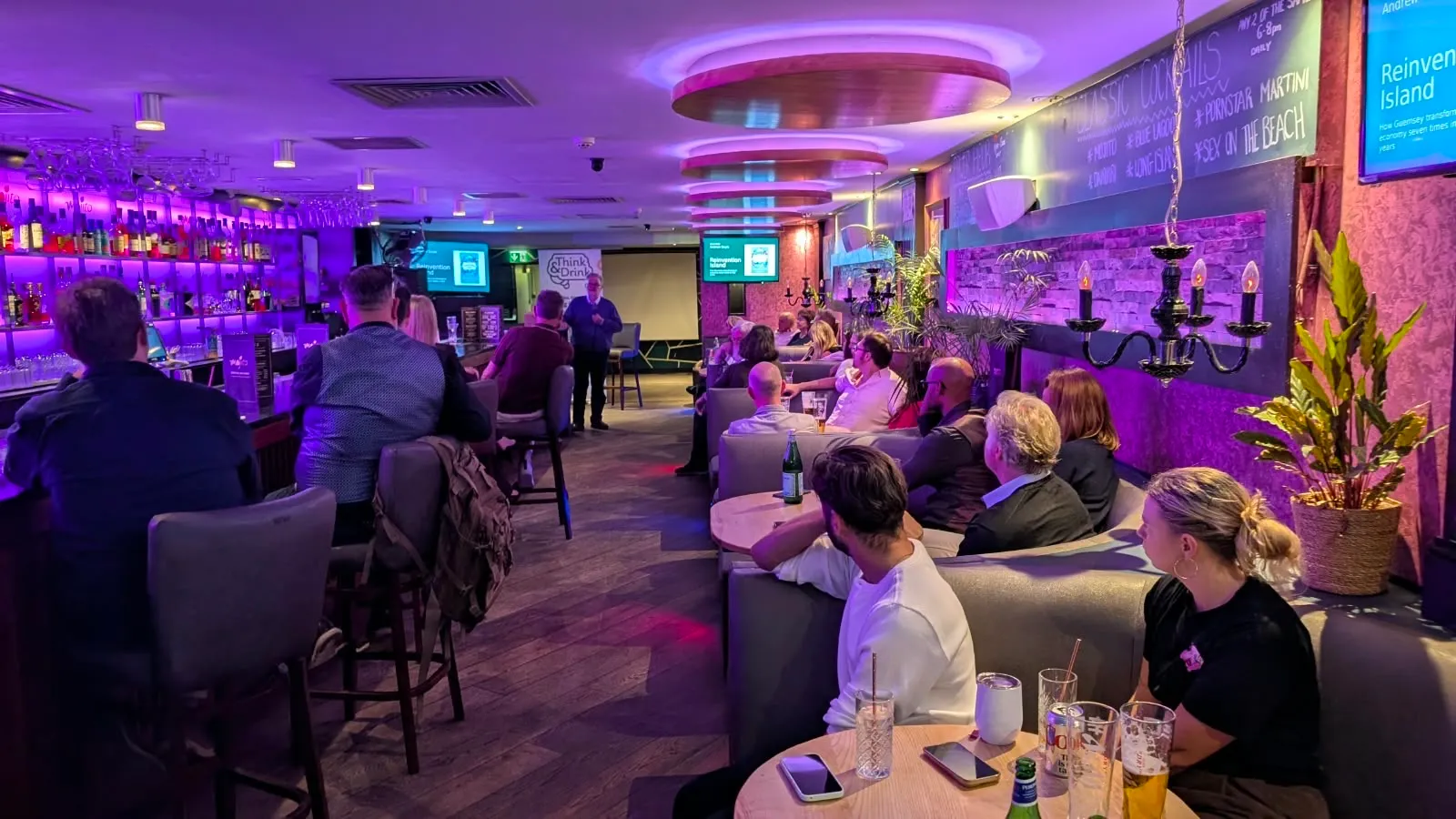 Andrew Doyle presenting Reinvention Island to a room of people at tables with drinks