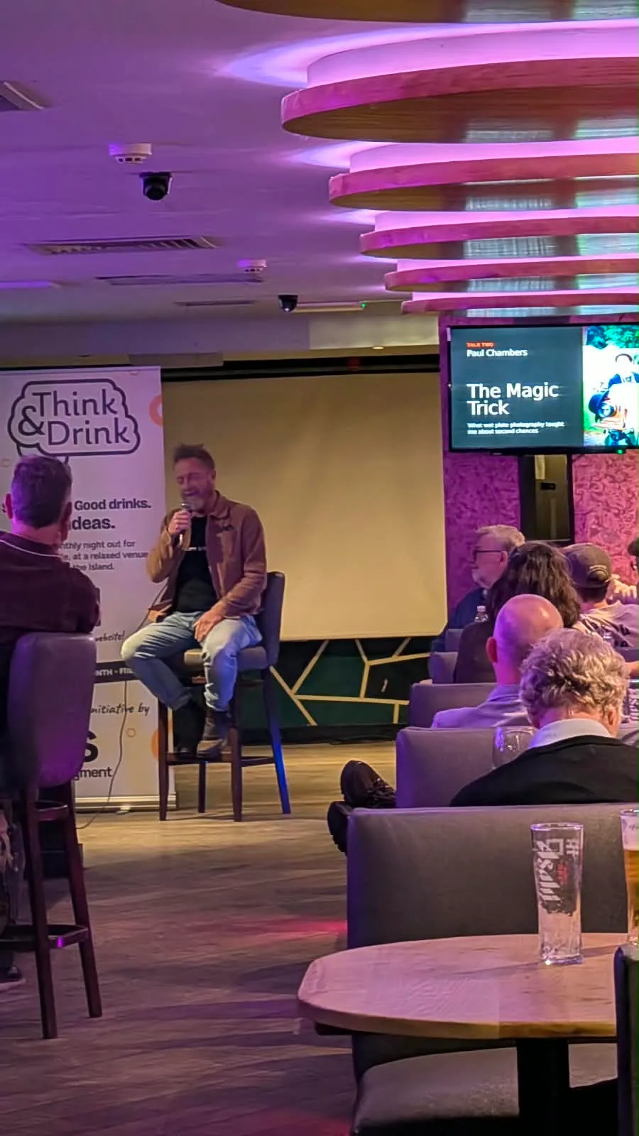 Paul Chambers on a stool with a microphone, his talk title The Magic Trick on the screen